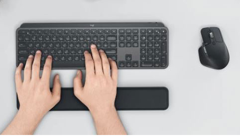 Two hands are placed upone a keyboard and palm rest which are next to a mouse